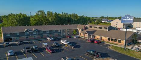 A parking lot with multiple vehicles, a building with a sign reading "AmericInn by Wyndham", and a large truck with an advertisement.