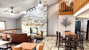 A restaurant with a stone fireplace, wooden furniture, and a high ceiling with fans. - AmericInn by Wyndham Ames (Ames)