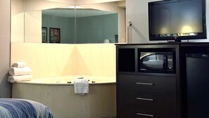 A hotel room with a bed, a vanity with a mirror, a television, and a microwave. - AmericInn by Wyndham Ames (Ames)