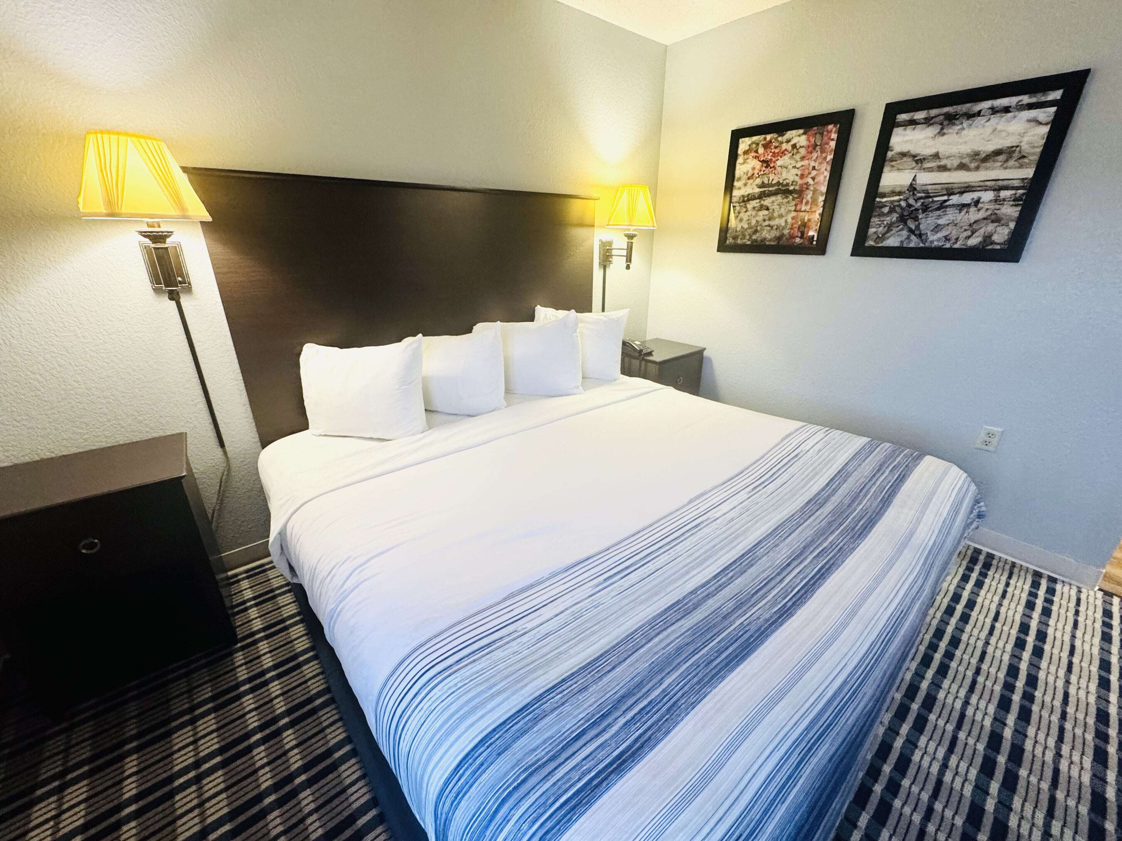 Une chambre d’hôtel avec un grand lit, deux lampes de chevet, une tête de lit et deux tableaux encadrés au mur.