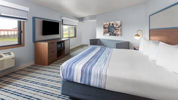 A hotel room with a large bed, a flat-screen TV mounted on the wall, a desk with a chair, and a window with a view of the outside.
