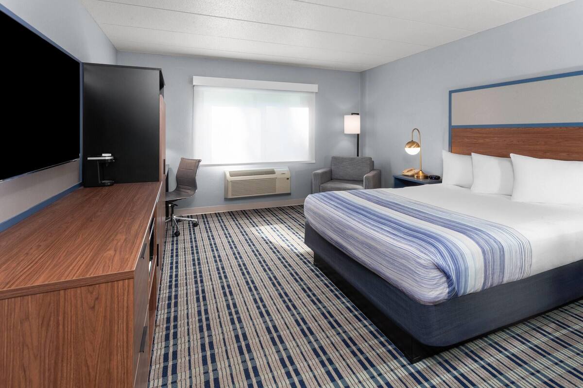 Een hotelkamer met een groot bed, een bureau, een stoel, een televisie, een lamp en een raam.