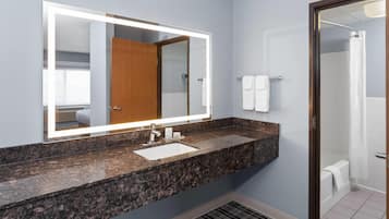 A bathroom with a granite countertop sink, a large mirror, a shower, and a towel rack.
