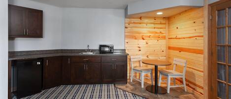 Una cocina compacta con armarios de madera oscura, microondas integrado y un pequeño comedor con dos sillas y una mesa.