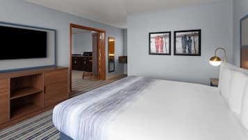 A hotel room with a large bed, a flat-screen TV mounted on the wall, a wooden dresser, and a mirror. There are two framed pictures on the wall.