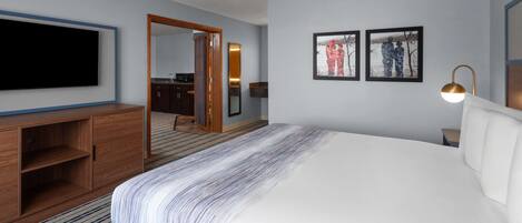 Une chambre d’hôtel avec un grand lit, un téléviseur à écran plat fixé au mur, une commode en bois et un miroir. Deux tableaux encadrés sont accrochés au mur.
