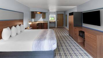 Quarto de hotel com cama grande, televisão, pequena cozinha e banheiro.