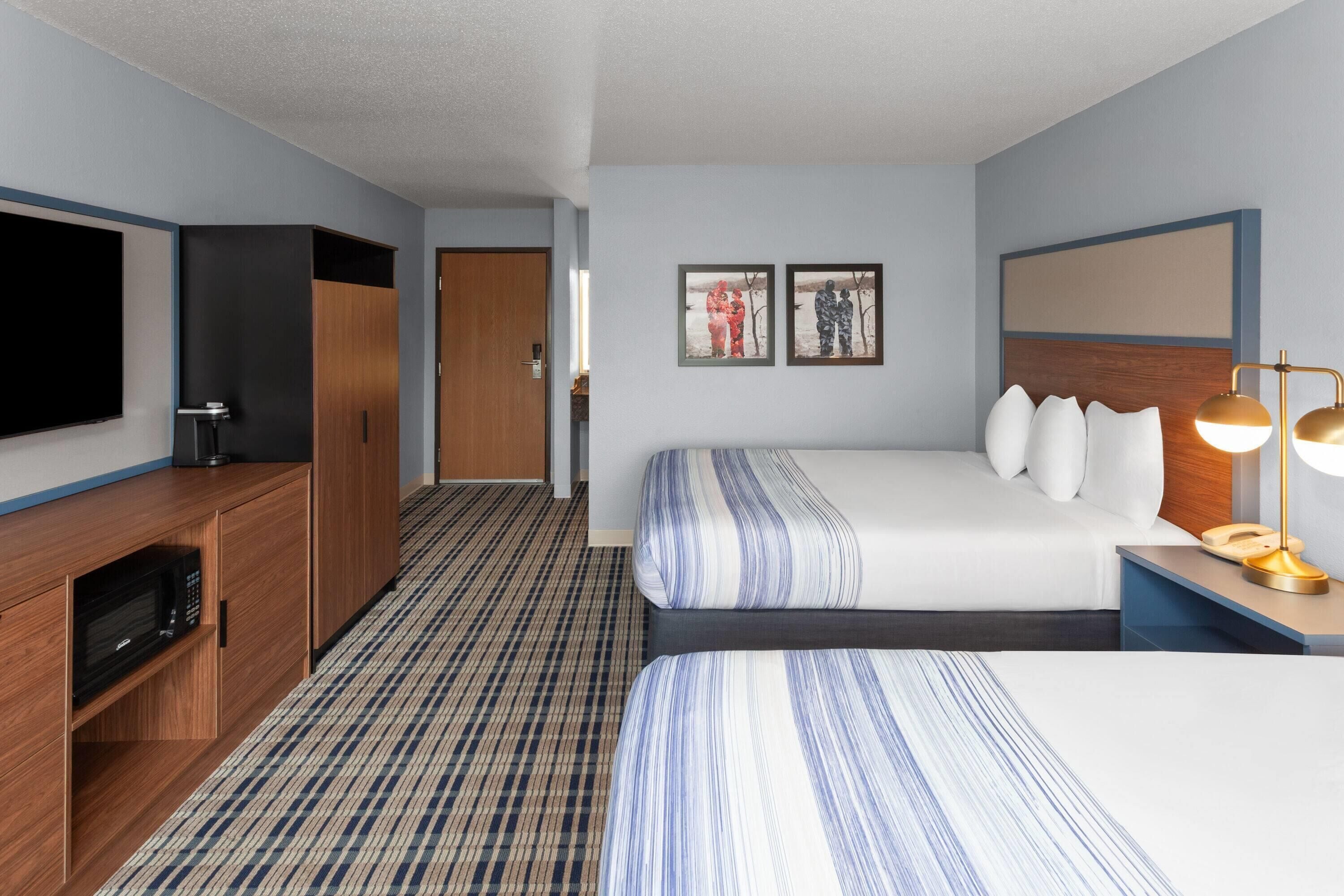 A hotel room with a bed, a TV, a desk with a lamp, and a microwave.