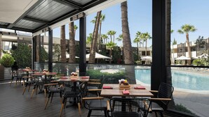 An outdoor dining area with tables and chairs, overlooking a pool and palm trees. - Amman Marriott Hotel (Amman)