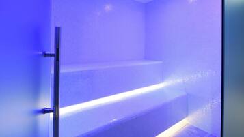 Une salle de bain avec une zone de douche éclairée en bleu, une porte en verre et des murs carrelés.