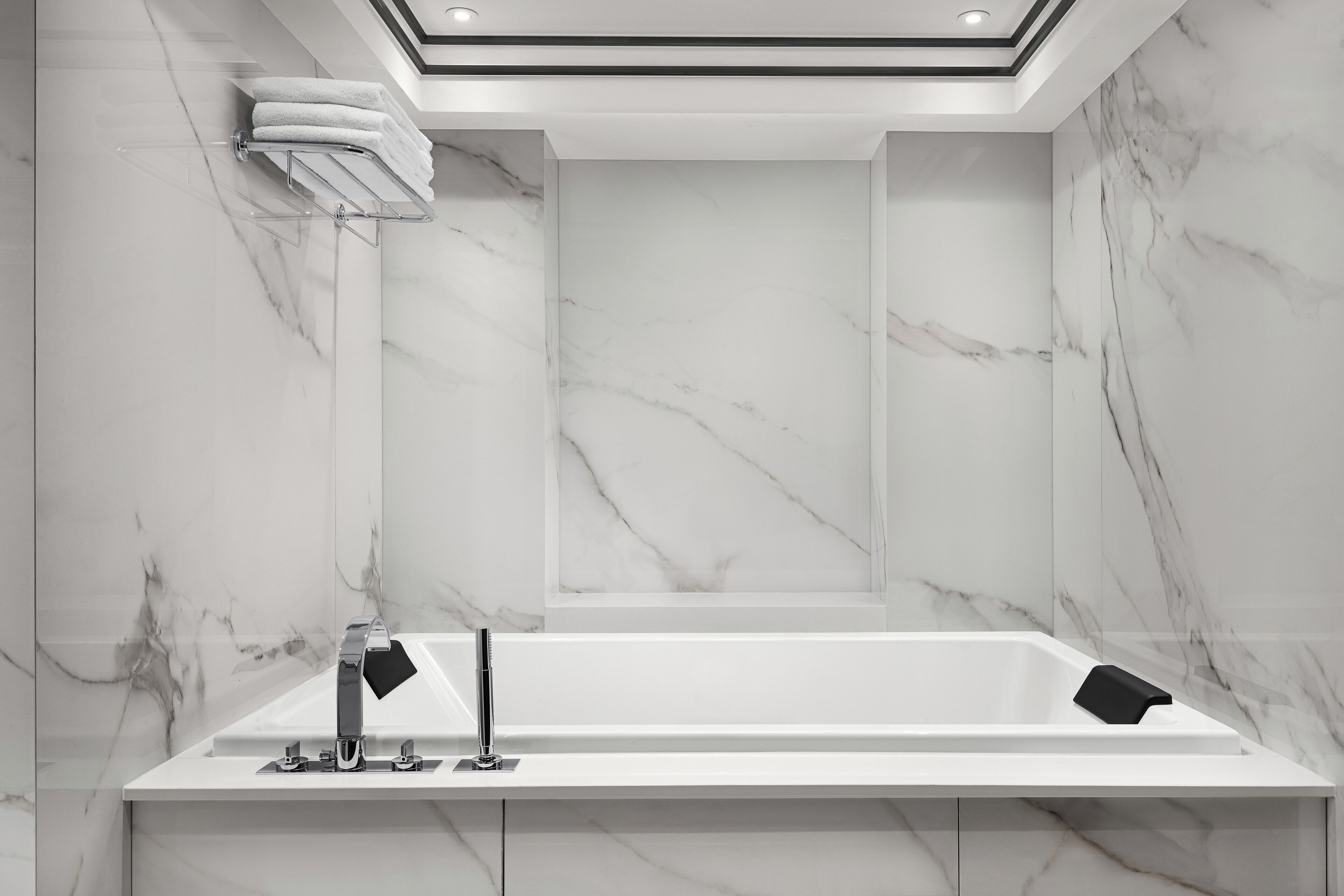 A modern bathroom with a marble wall, a white bathtub, and a sleek faucet.