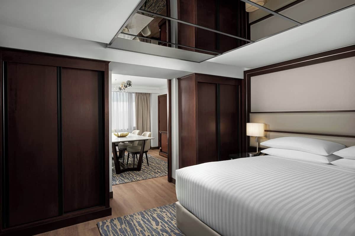 Ein Hotelzimmer mit einem großen Bett, einem Schreibtisch mit Stühlen und Blick auf den Flur.