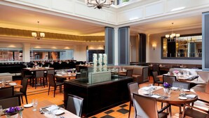A spacious hotel dining area with multiple tables and chairs, a central bar area, and large windows allowing natural light. - Amman Marriott Hotel (Amman)