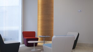 Un espacio lounge moderno con una butaca roja, una mesa blanca y una silla tapizada en azul.