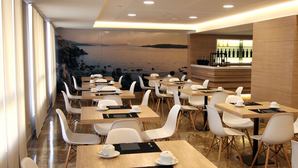 Un restaurante moderno con un mural costero, mesas y sillas ordenadas y una zona de bar.