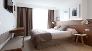 Una habitación de hotel moderna con una cama grande, un escritorio, una silla, una mesita y una lámpara de noche.