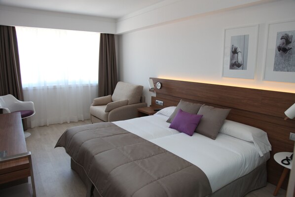 A hotel room with a large bed, a desk, a chair, a nightstand, and a window with curtains. - Hotel Gelmírez (Santiago de Compostela)