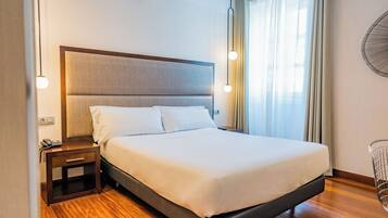 Una habitación de hotel moderna con una cama grande, mesita de noche con teléfono y ventilador de pared.
