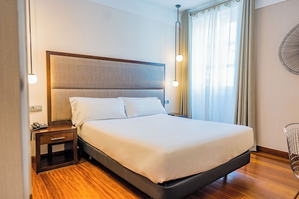 Una habitación de hotel moderna con una cama grande, mesita de noche con teléfono y ventilador de pared.
