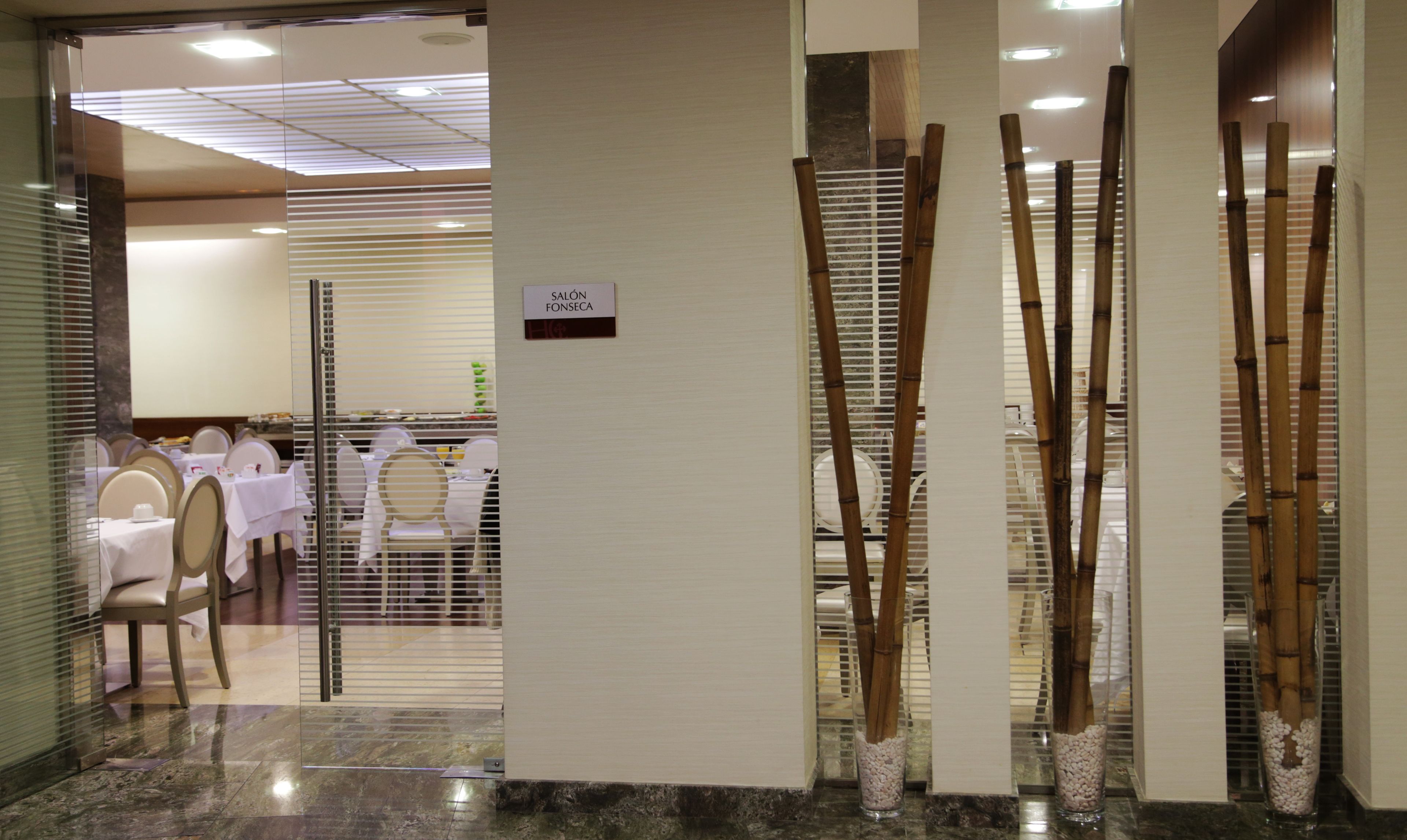 A hotel reception area with a sign reading "SALÓN FORSECA". There are tables and chairs set up for dining, and decorative bamboo plants in vases.
