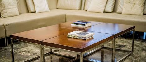 A modern living room with a wooden coffee table, a sofa with cushions, and a stack of books on the table.