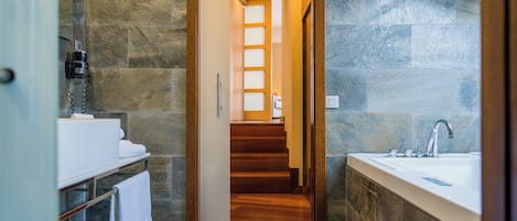 Un baño moderno con una escalera de madera que sube a un segundo piso, una bañera grande y un lavabo blanco.
