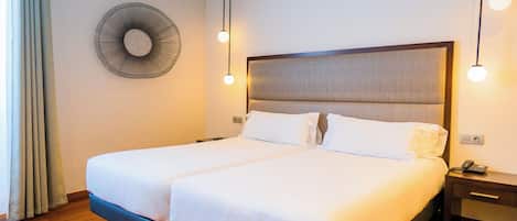 A double bed with a wooden headboard, two bedside tables, a wall-mounted fan, and a telephone on the right side.