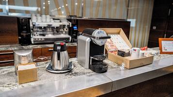 Eine Kaffeemaschine, eine Kaffeekanne und eine Schachtel mit Kaffeekapseln auf einer Marmorarbeitsplatte.