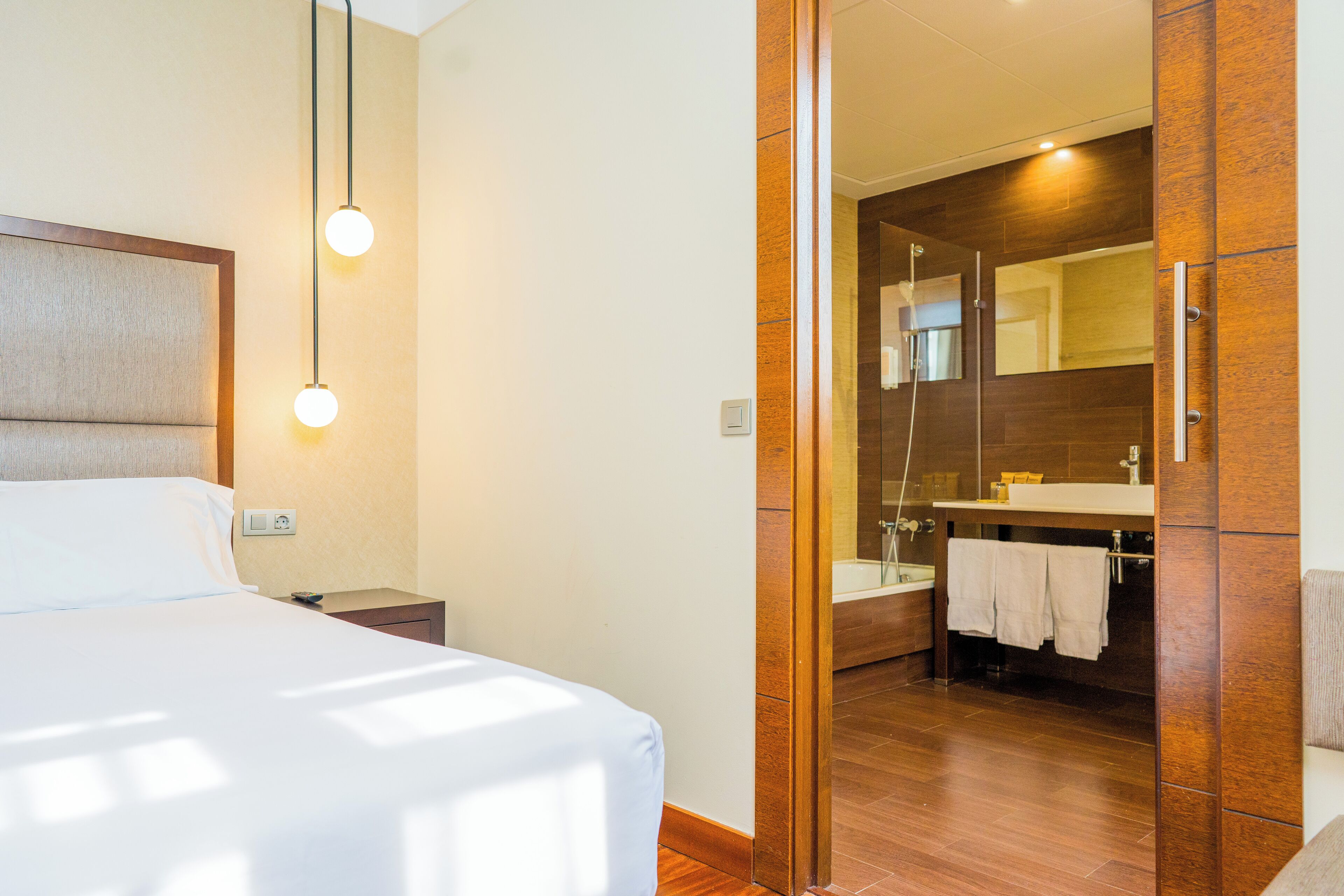 A modern hotel room with a large bed, bedside table, and a wooden-framed mirror.
