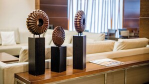 Un área de recepción con un mostrador de madera, dos esculturas metálicas decorativas sobre pedestales negros y un sofá blanco al fondo.