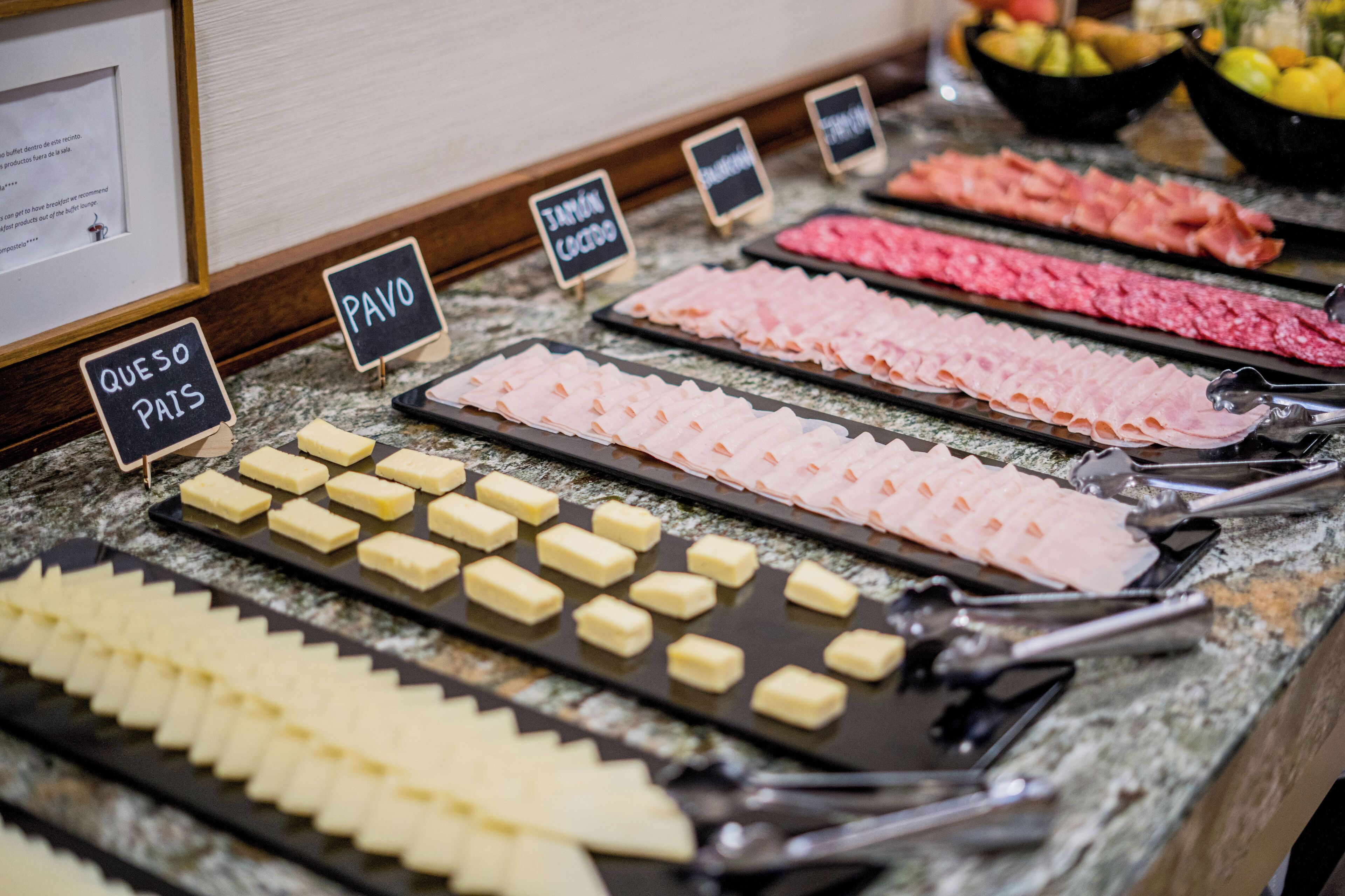 Un bufé con diversos alimentos, incluyendo queso, jamón y otras carnes frías.