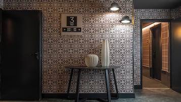 A hotel interior with a patterned wall, a sign indicating the 3rd floor, a table with two vases, and a door to the left.