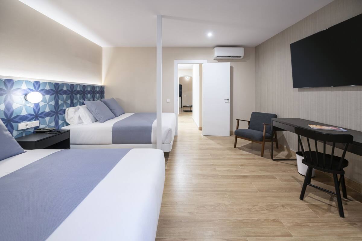 A hotel room with two beds, a desk, a chair, and a TV.