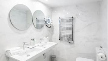 Ein modernes Badezimmer mit einem Doppelwaschbecken, zwei runden Spiegeln, einem Handtuchhalter, einer Toilette und einem Papierkorb.