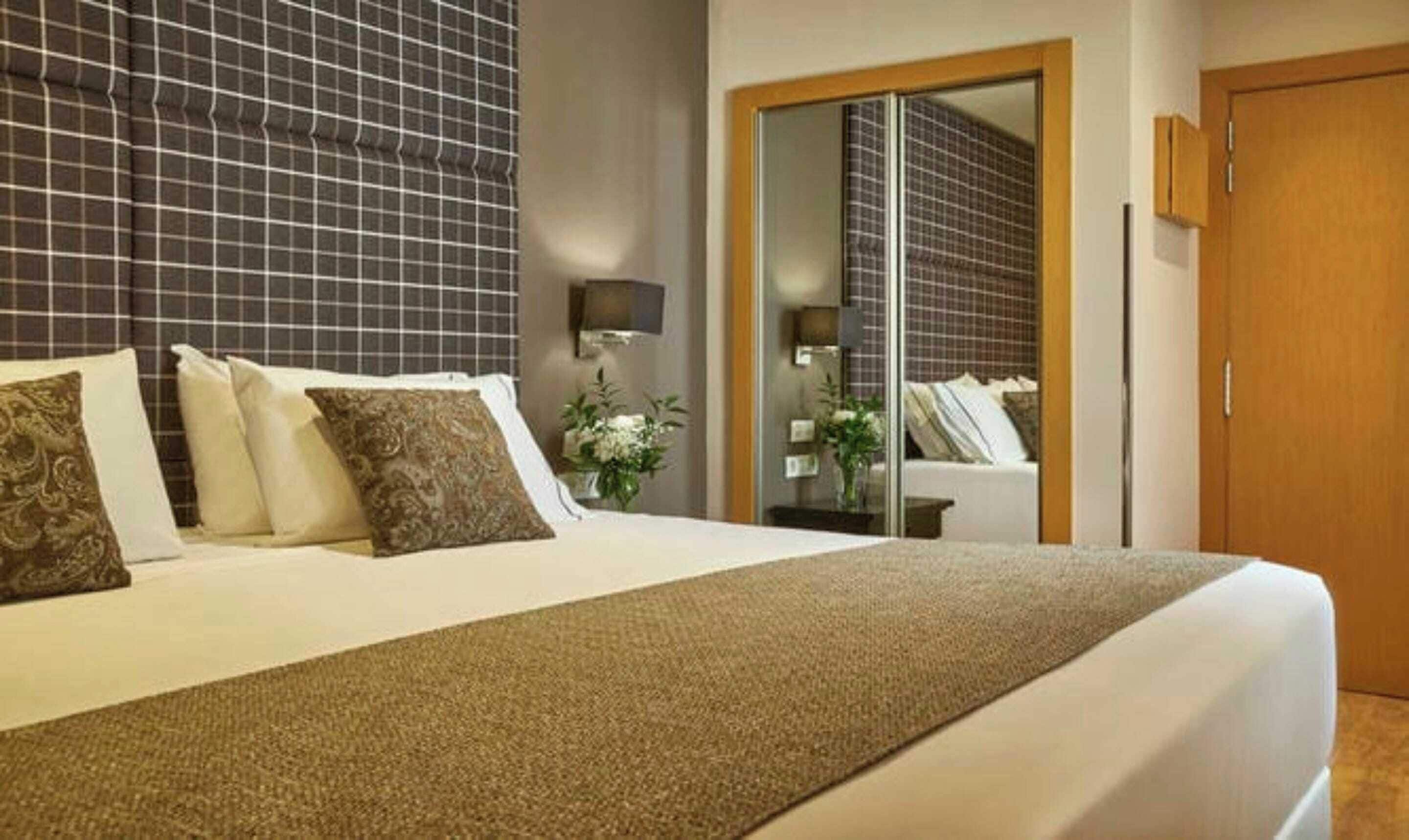 A hotel room with a large bed, a wardrobe, a mirror, and a small table with a plant.