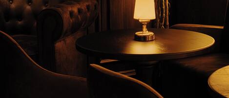 Una habitación con poca luz, una mesa redonda, una silla, una lámpara y un sofá de cuero.