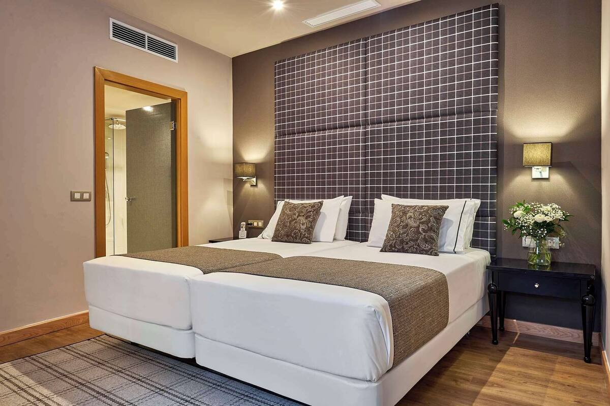 A hotel room with a large bed, two bedside tables, a nightstand, a mirror, and a wall-mounted light fixture.