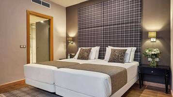 A hotel room with a large bed, two bedside tables, a nightstand, a mirror, and a wall-mounted light fixture.