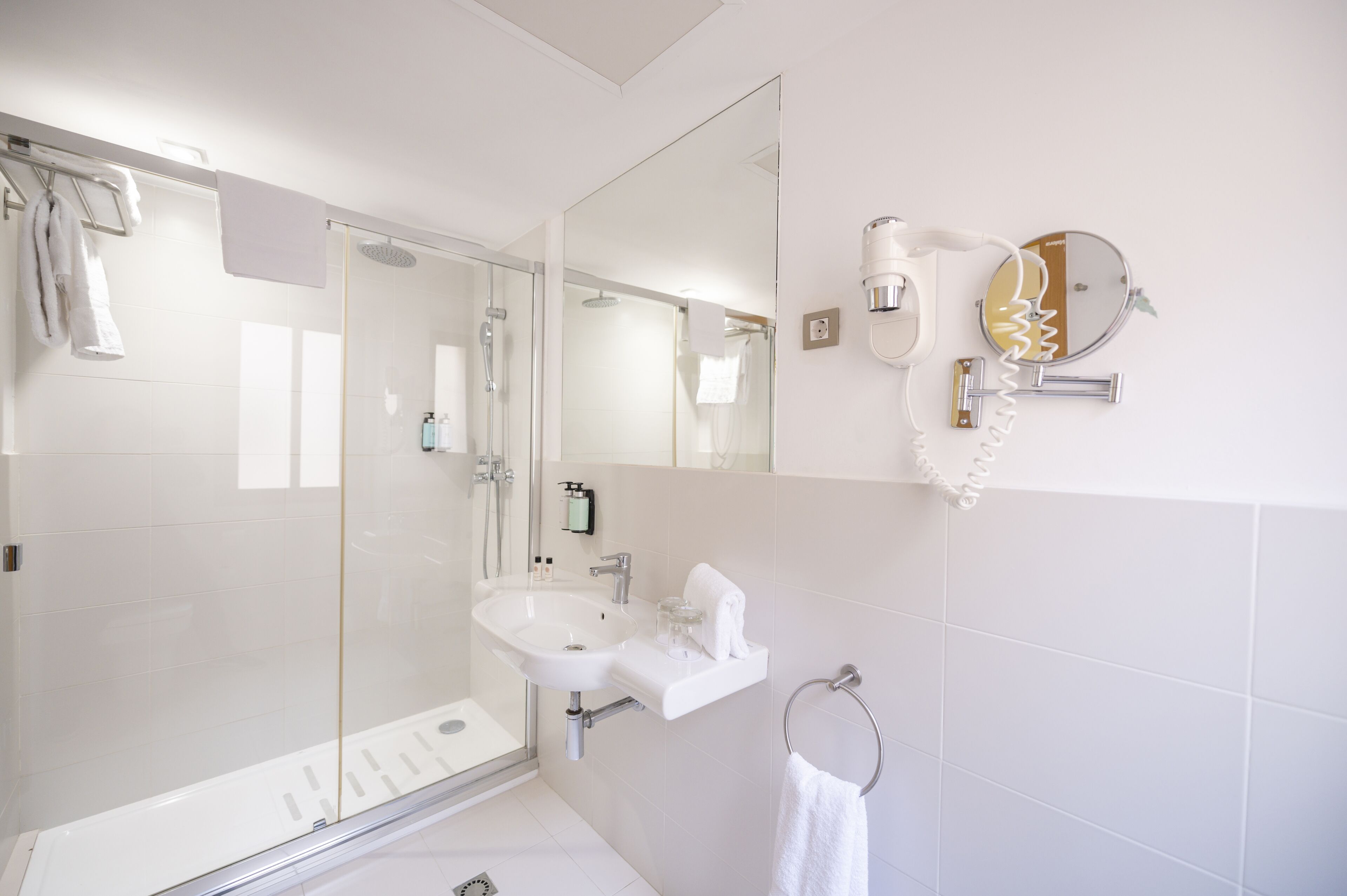 Un baño moderno con cabina de ducha de vidrio, un lavabo blanco y un espejo con teléfono.