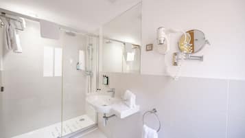 Une salle de bain moderne avec une douche à parois de verre, un lavabo blanc et un miroir doté d’un téléphone.