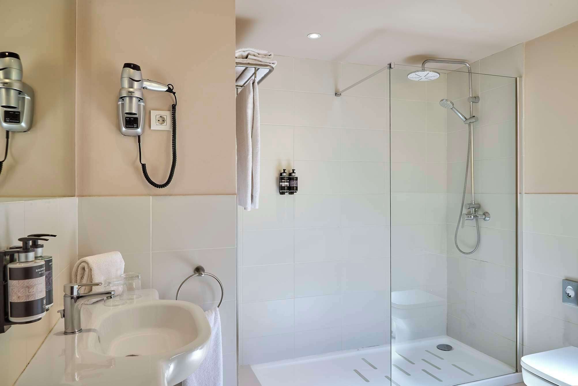 Een moderne badkamer met een douchecabine van glas, een wastafel met spiegel en een aan de muur bevestigde haardroger.