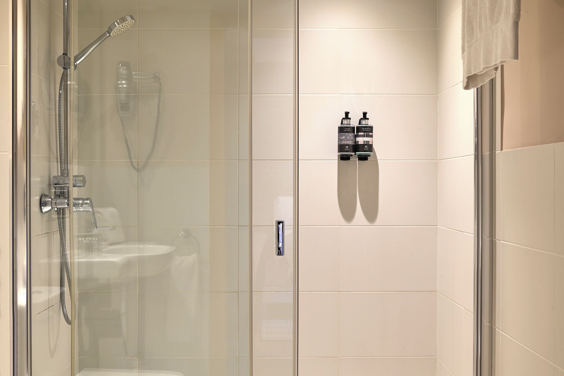 Un baño moderno con cabina de ducha de vidrio, un lavamanos y dos dispensadores de jabón para manos montados en la pared.