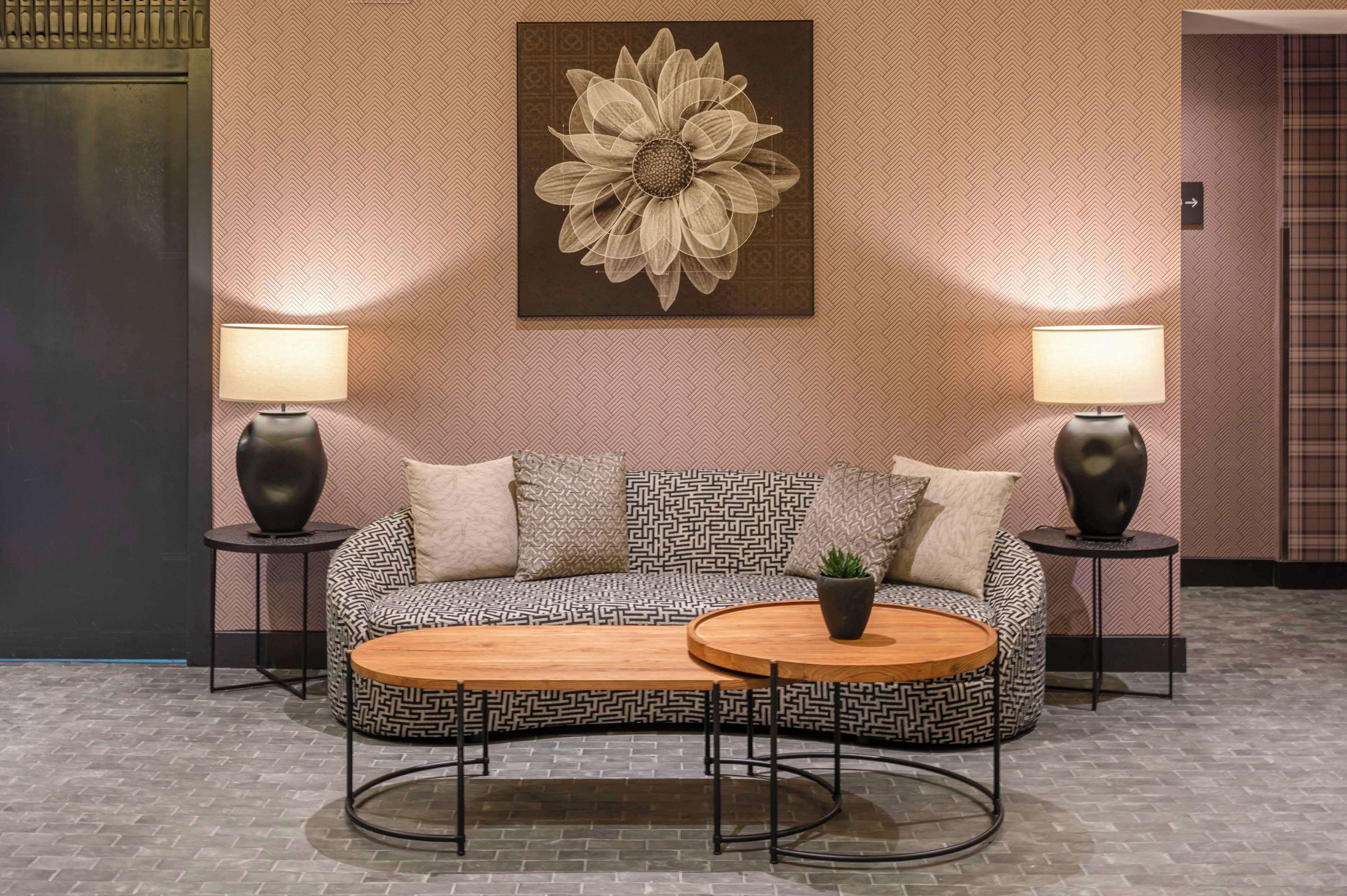 A modern lobby with a patterned sofa, two side tables with lamps, a coffee table, and a large floral artwork on the wall.