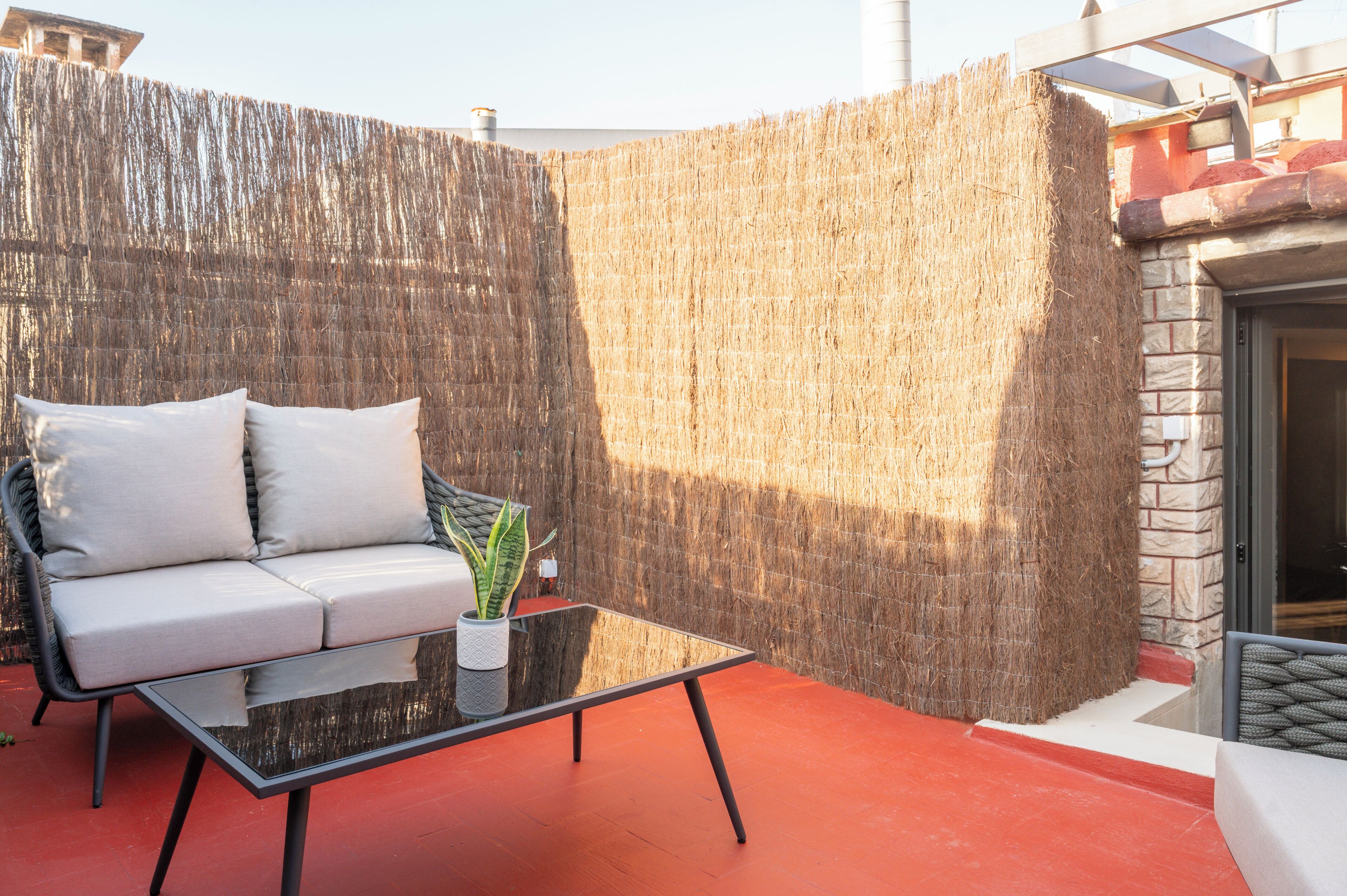 A modern outdoor seating area with a sofa, a glass table, and a potted plant.