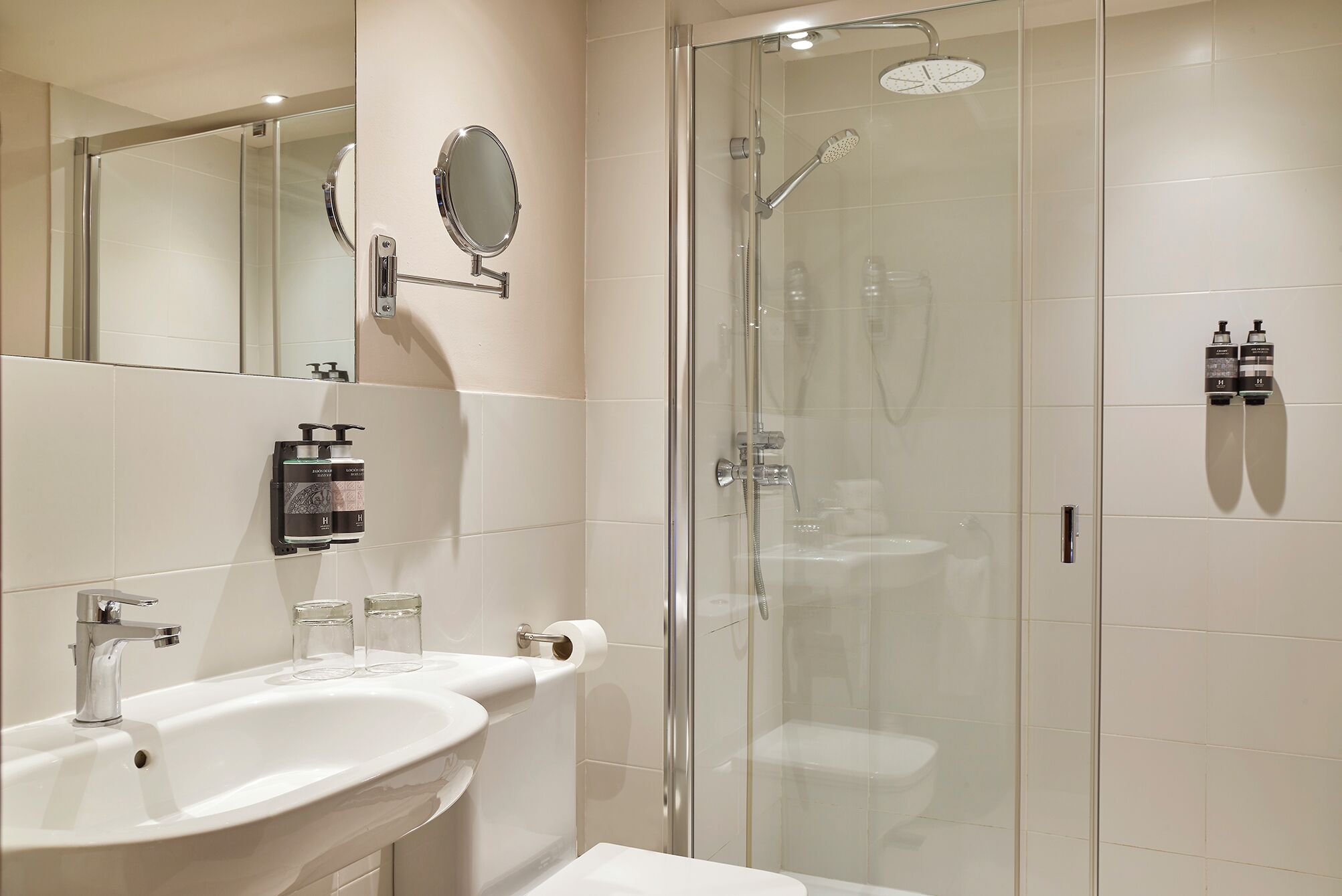 Un baño moderno con ducha envuelta en vidrio, un lavabo blanco y dos dispensadores de jabón para manos.