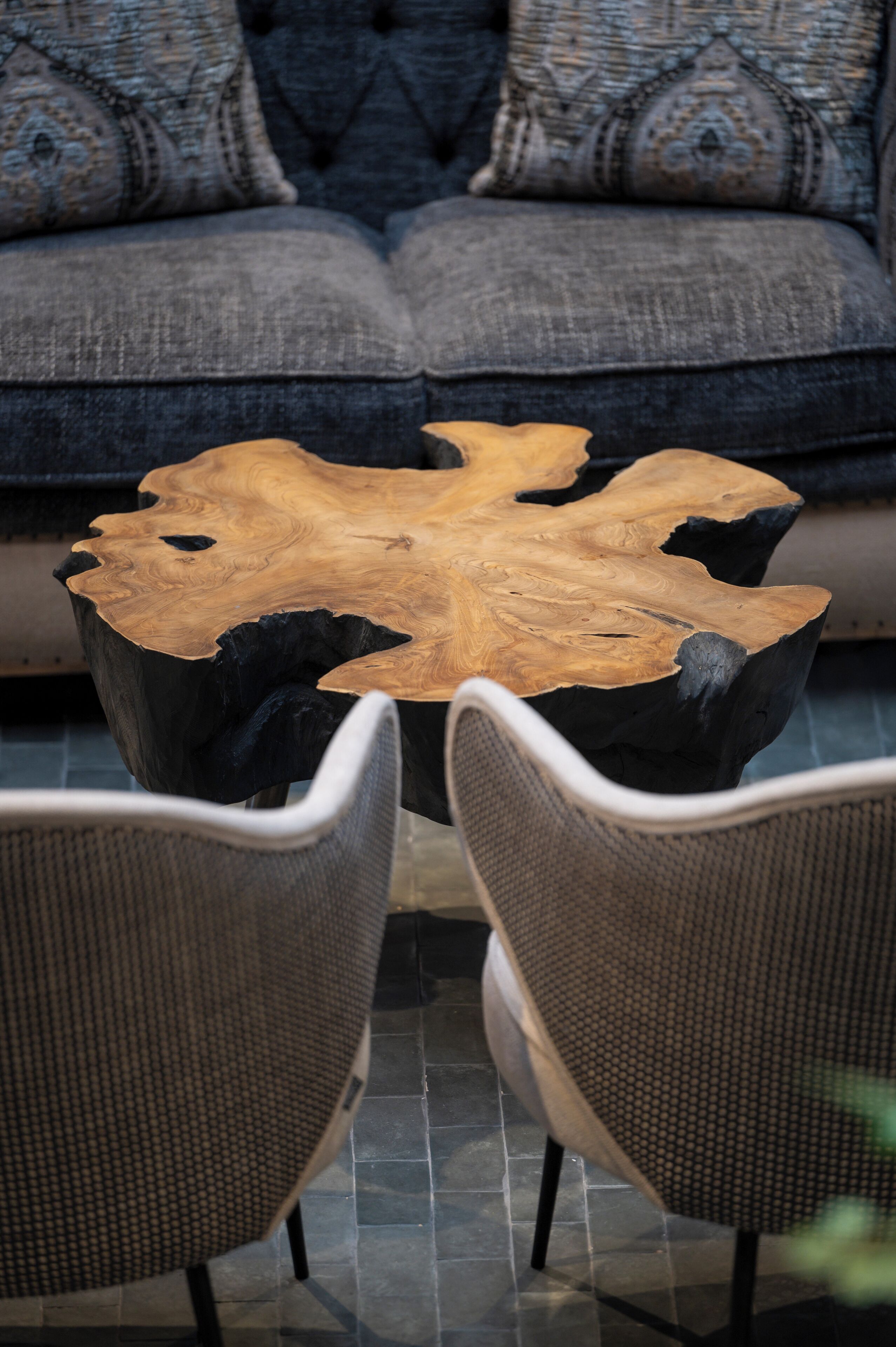 A round coffee table with a natural wood finish and black accents, placed between two wicker chairs.