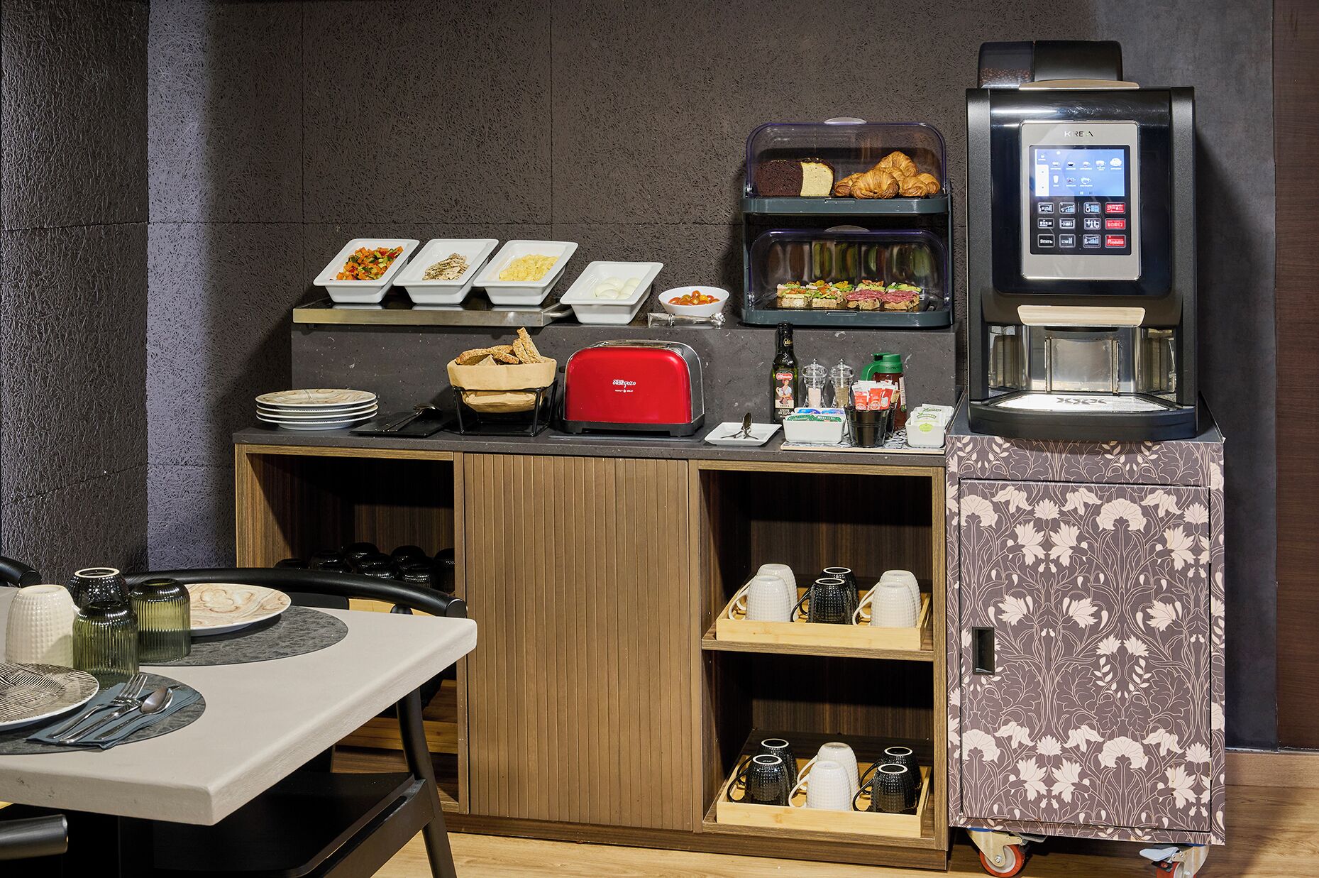 A breakfast bar with various food items, a coffee machine, and a beverage dispenser.