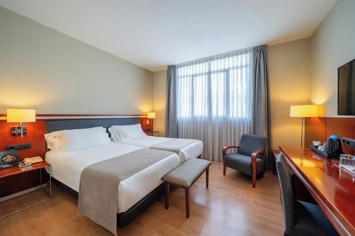Habitación de hotel con dos camas, un escritorio, una silla, un televisor y una ventana con cortinas.