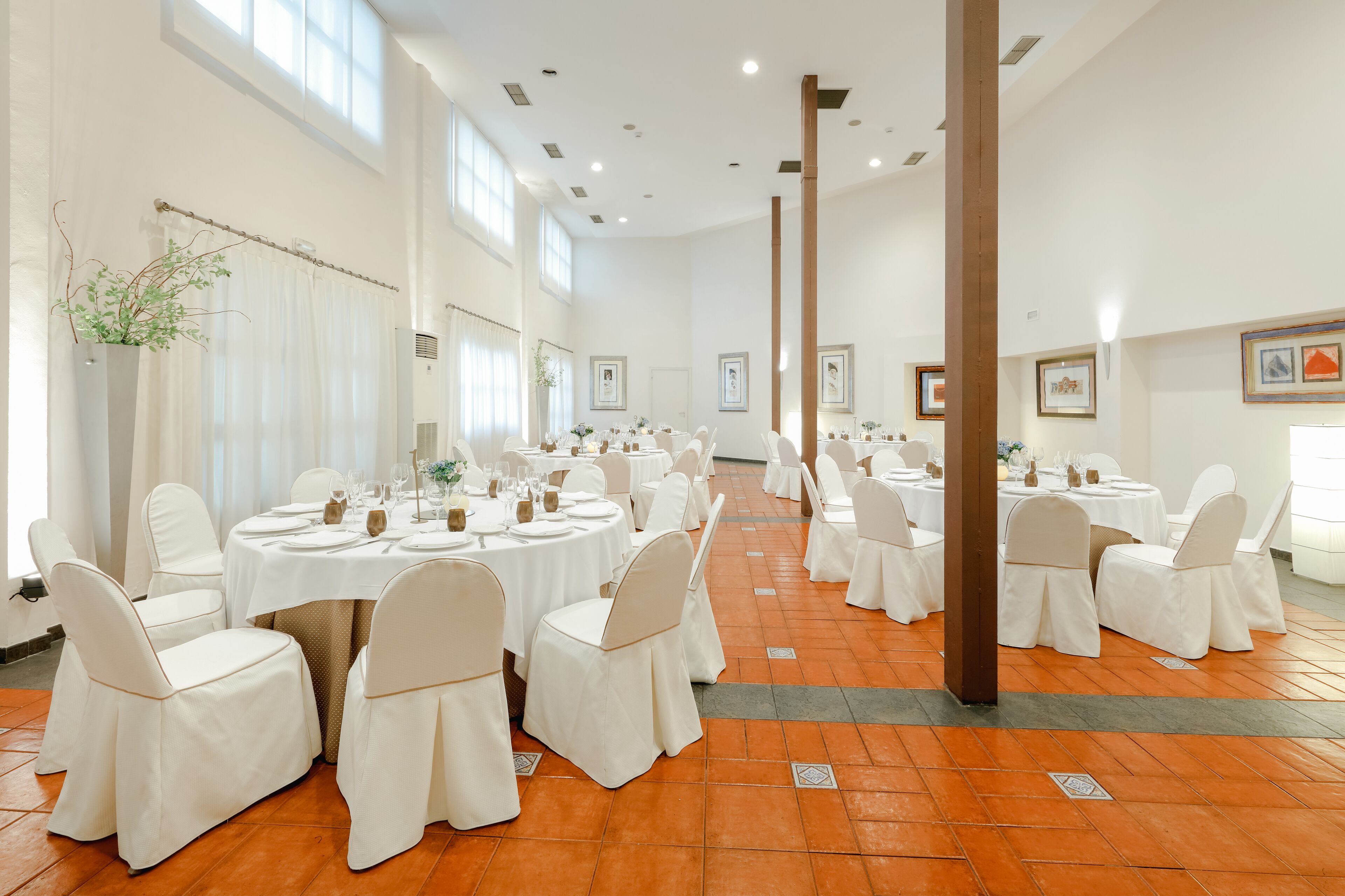 A spacious banquet hall with multiple round tables, white chairs, and a high ceiling.