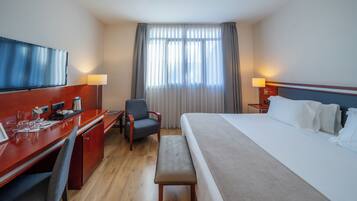 A hotel room with a bed, desk, chair, television, and curtains.